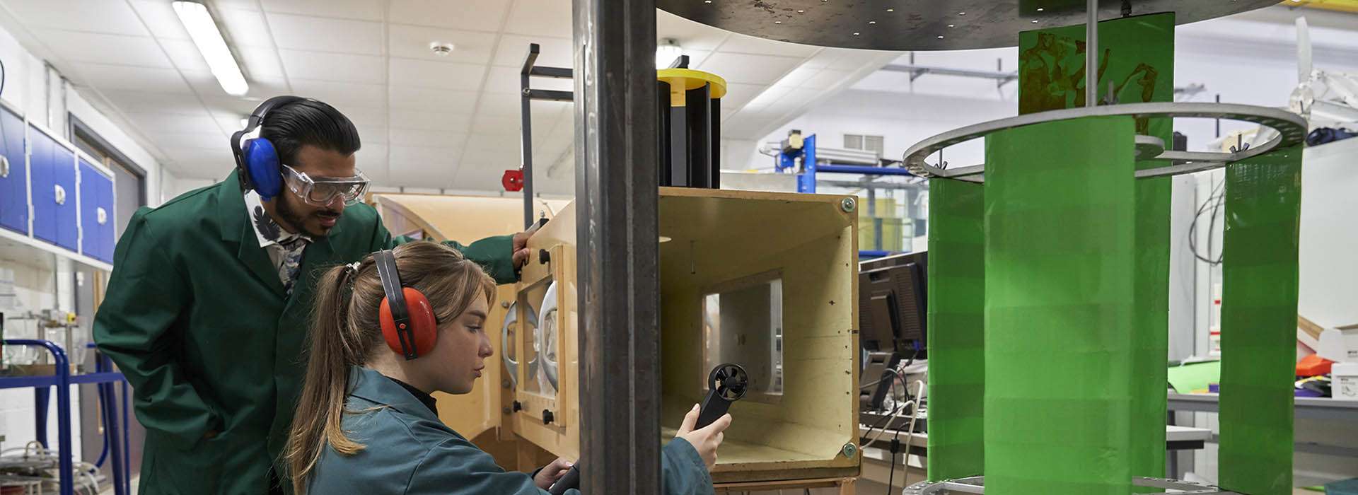 Two people in green overalls looking at engineering equipment