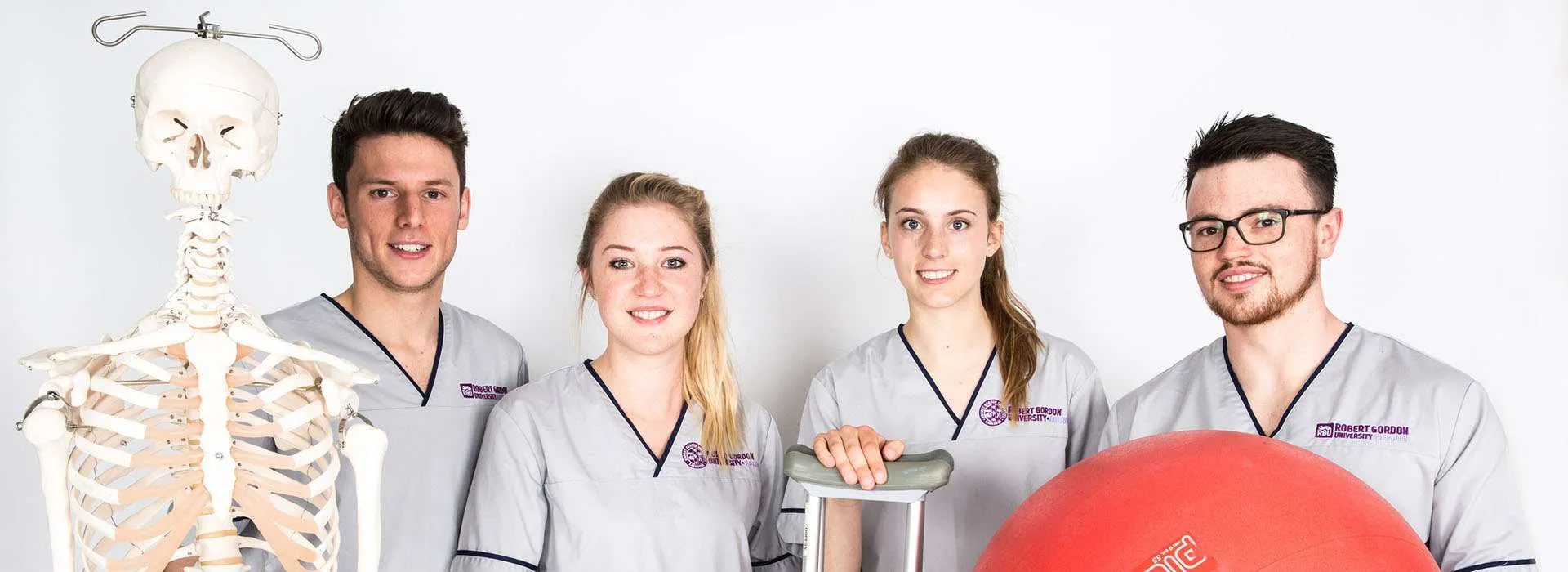 students wearing health uniforms next to a skeleton model