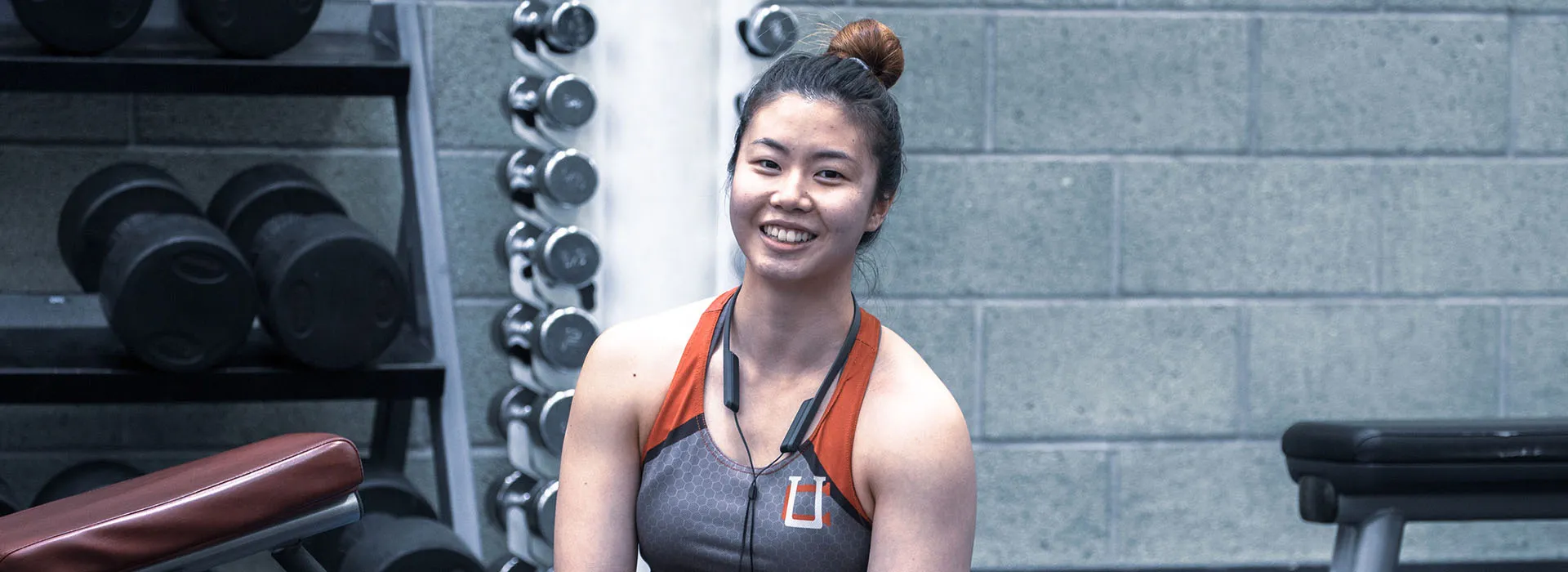 woman in workout gear sitting next to dumbells smiling