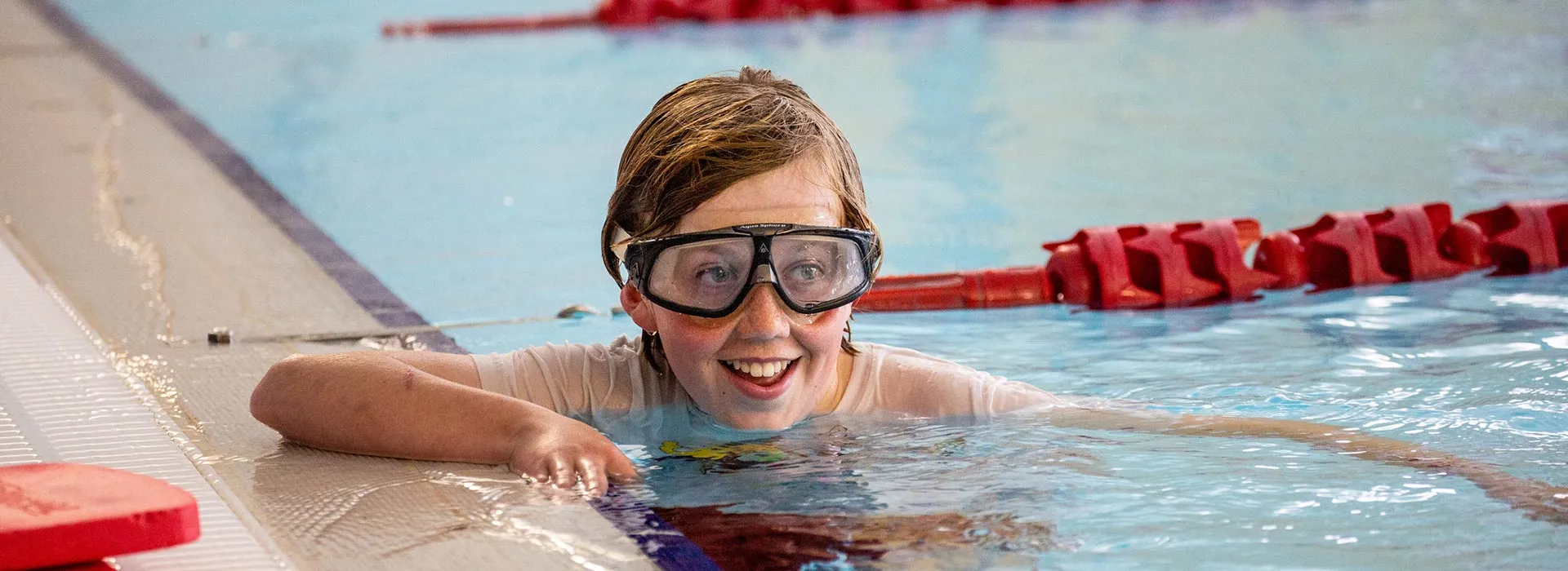child in a swimming pool smiling wearing goggles