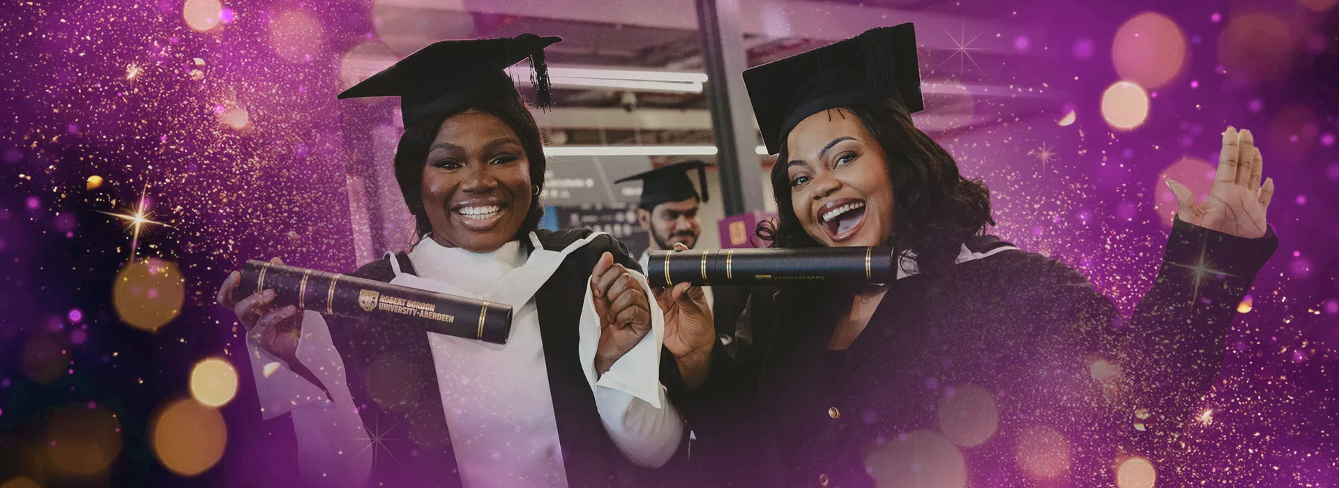 Two students hold up their graduation scrolls