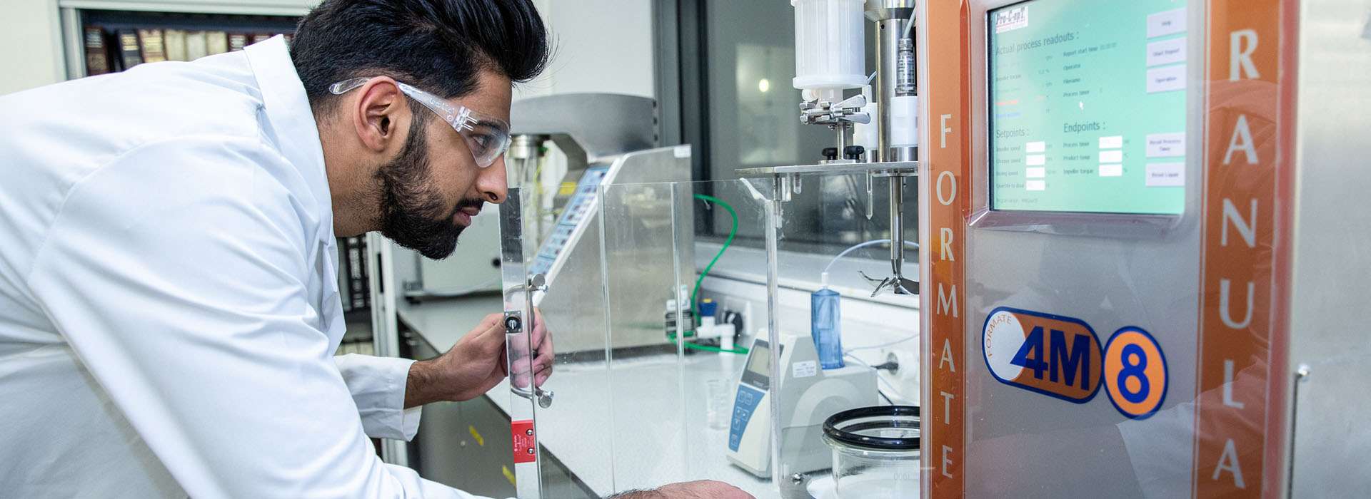 student in a lab coat looking at scientific equipment