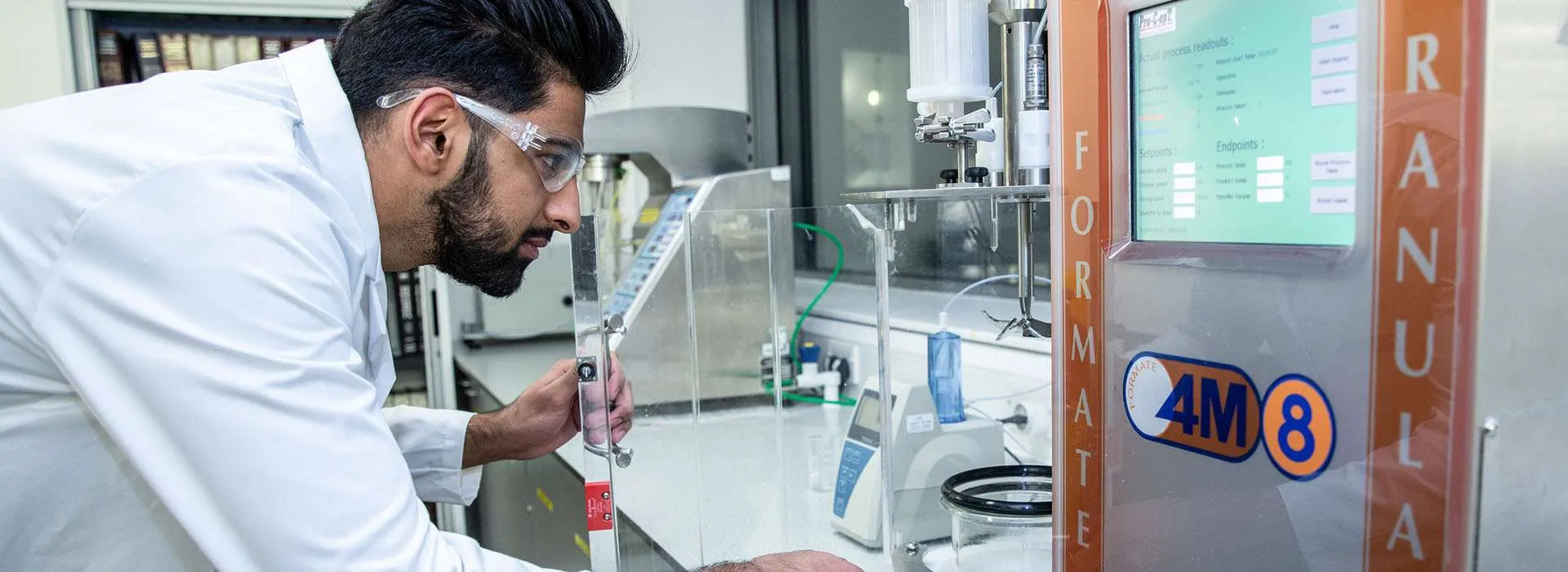 student in a lab coat looking at scientific equipment