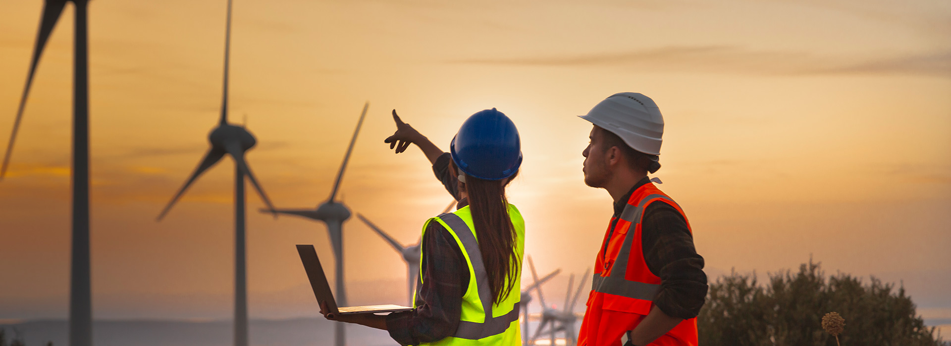 two people in yellow hi-vis jackets and hard hats are looking at some wind turbines