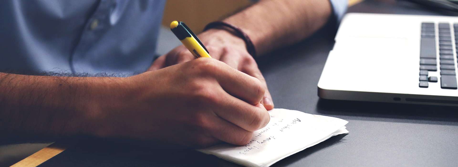 person taking notes next to their laptop