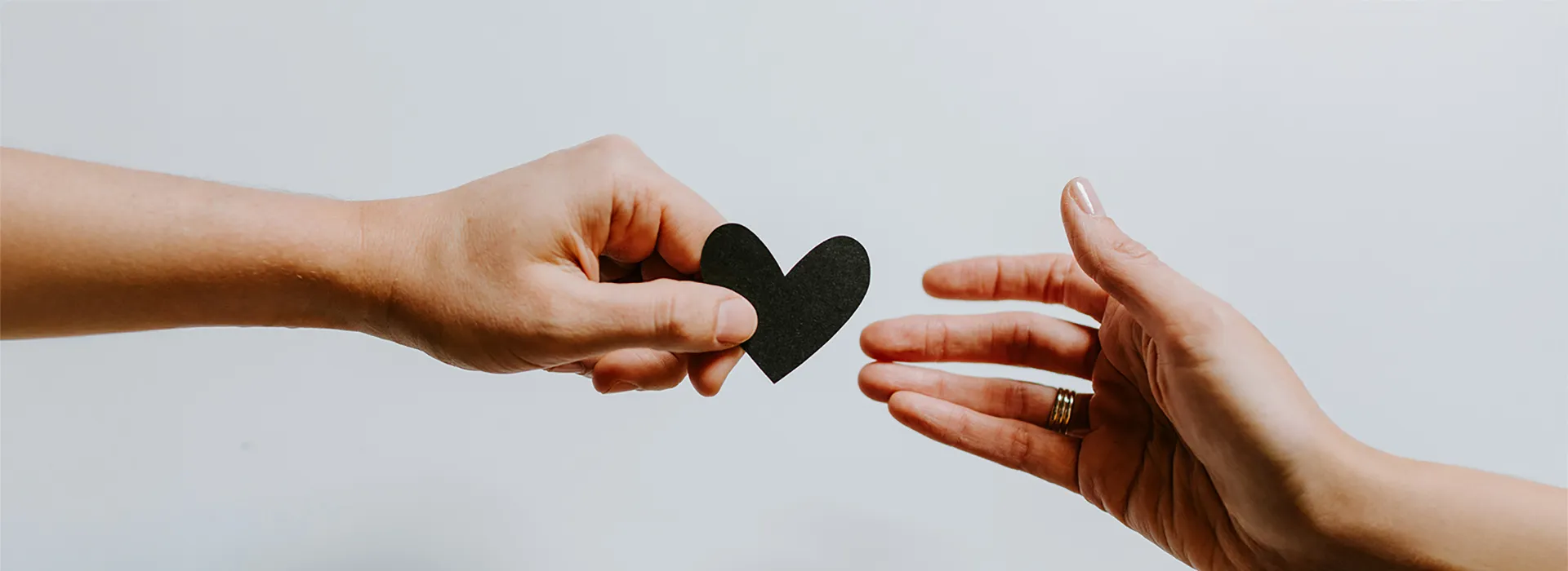 hand reaching for another hand with a paper cut out of a heart