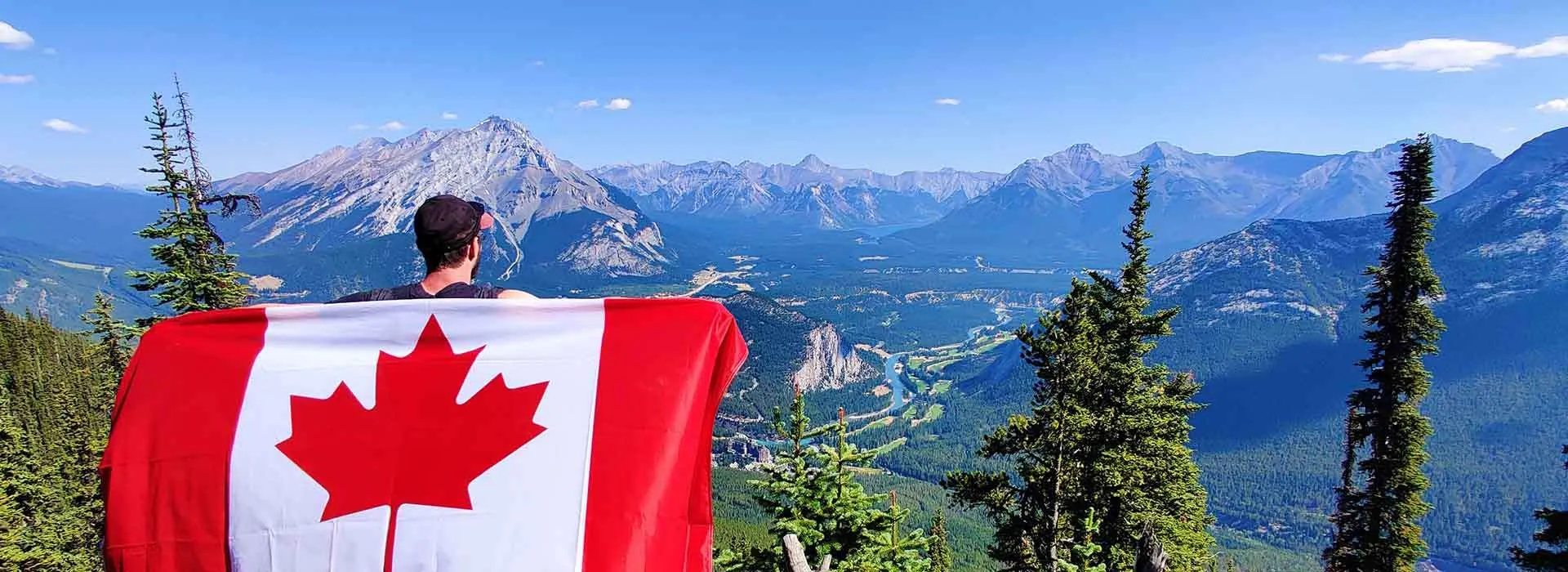 man holding canadian flag in front of mountainous vista