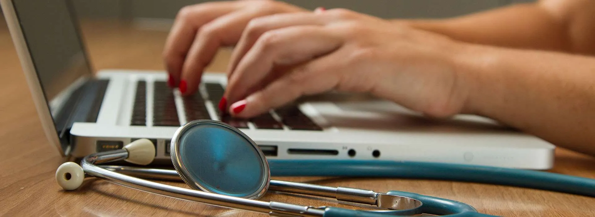 woman typing on a laptop with stethoscope on the desk