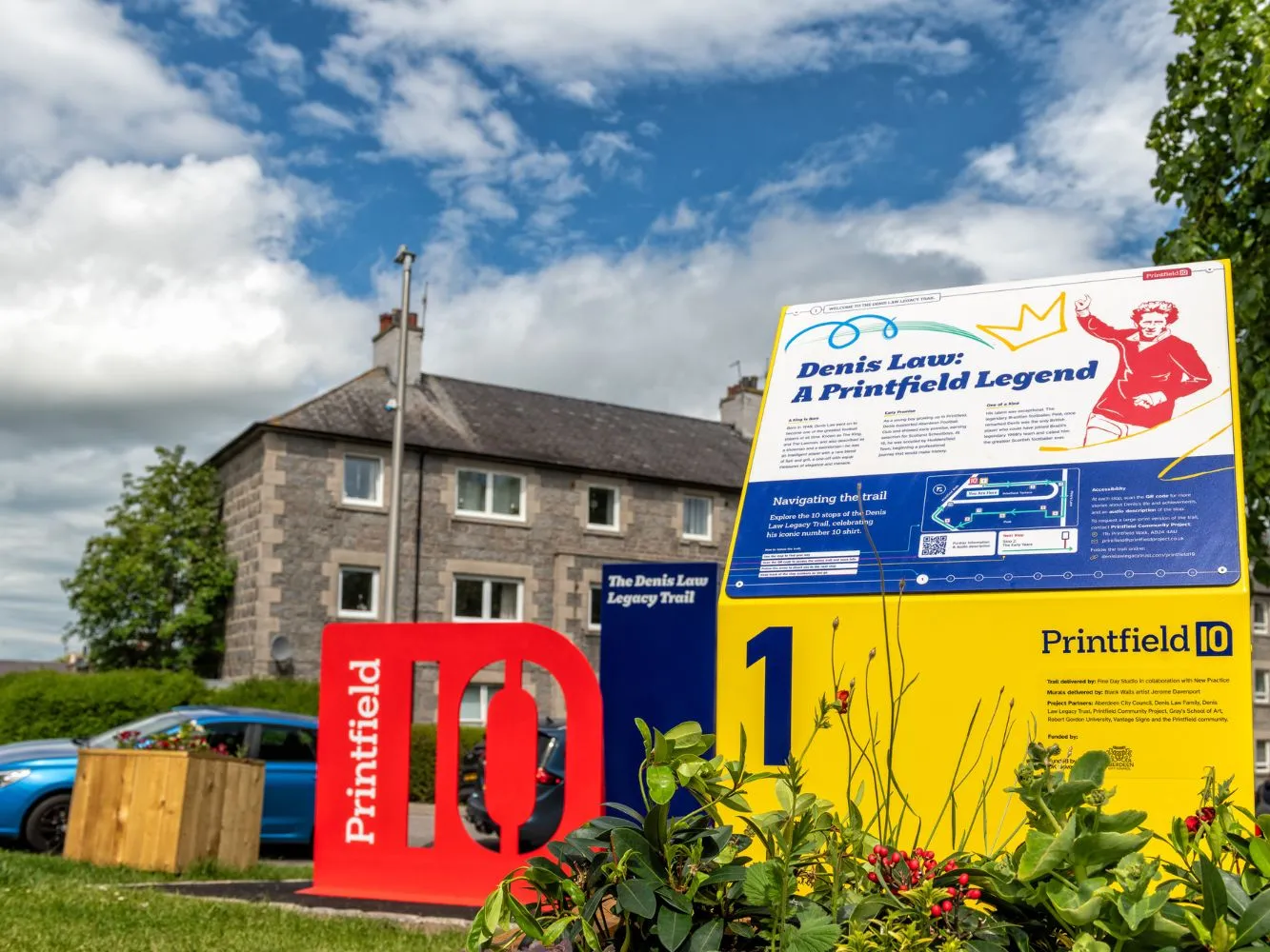 A Printfield 10 - Denis Law Legacy information board under a blue sky