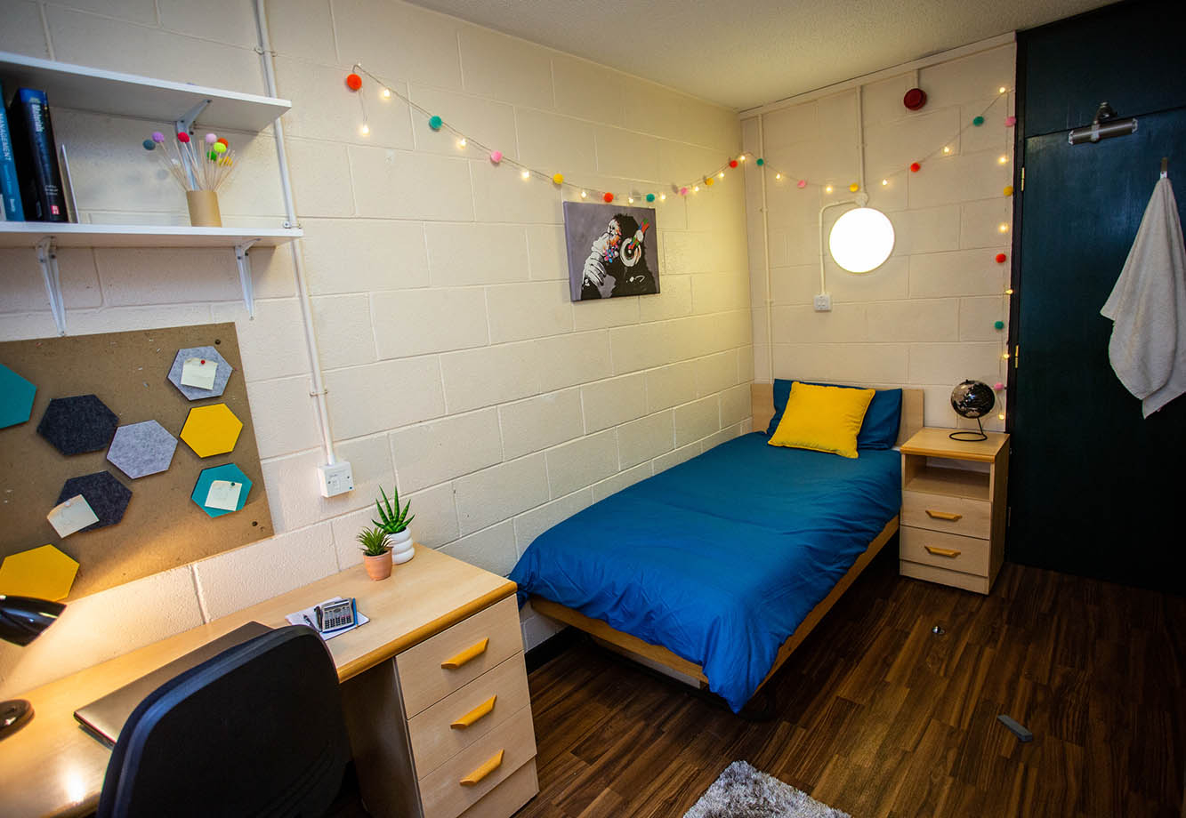 Bedroom featuring a single bed with blue sheets, fairy lights and a desk