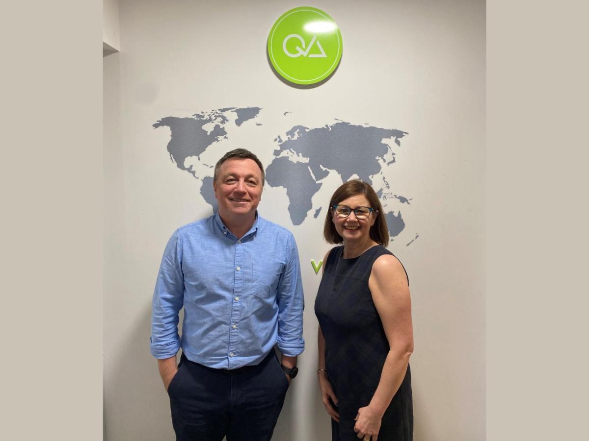 Steve Clark and Samantha Wallace, QA Travel, standing by a company logo