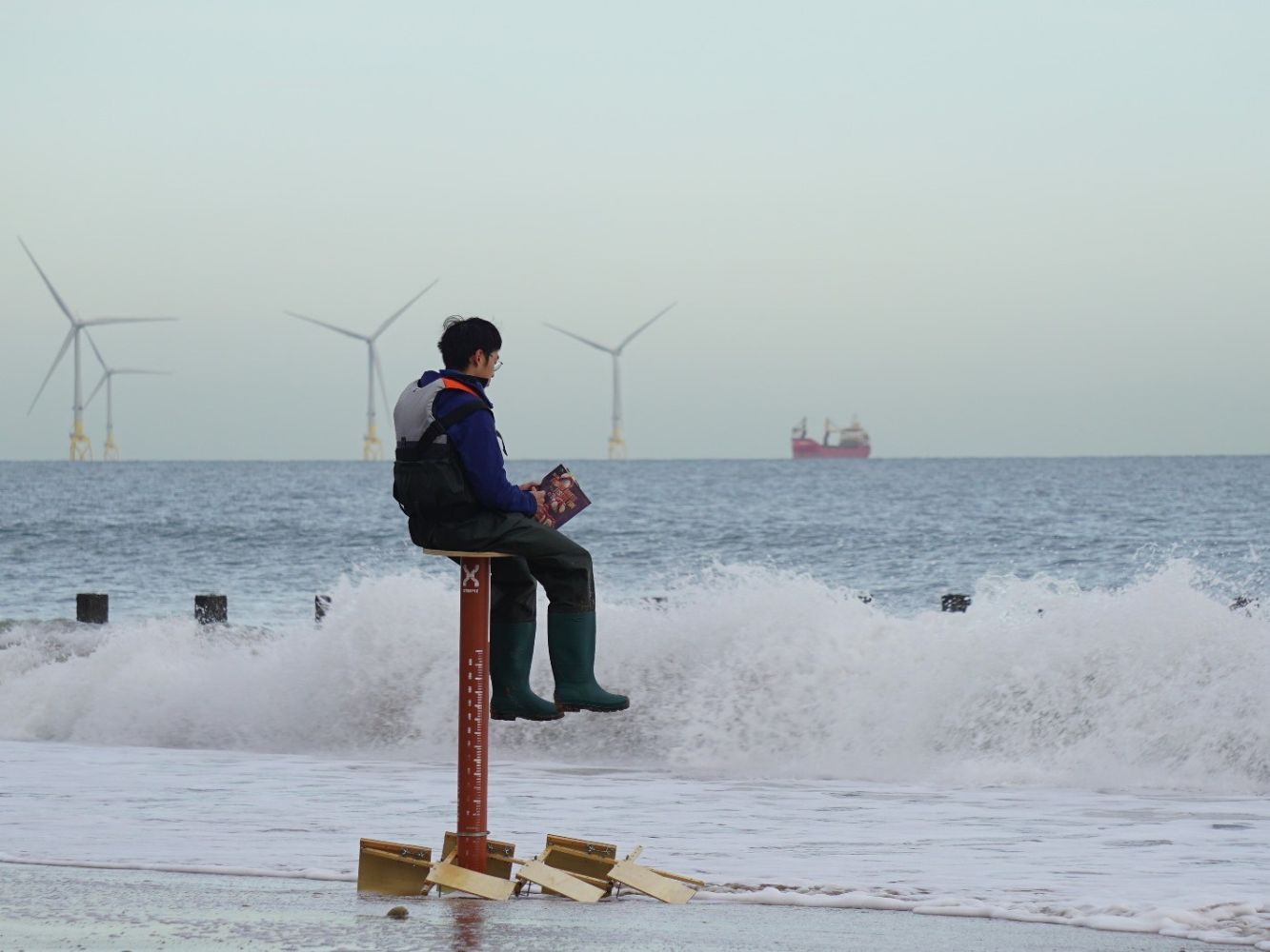 A man sits on a piece of architecture, on the sand looking out towards the North Sea