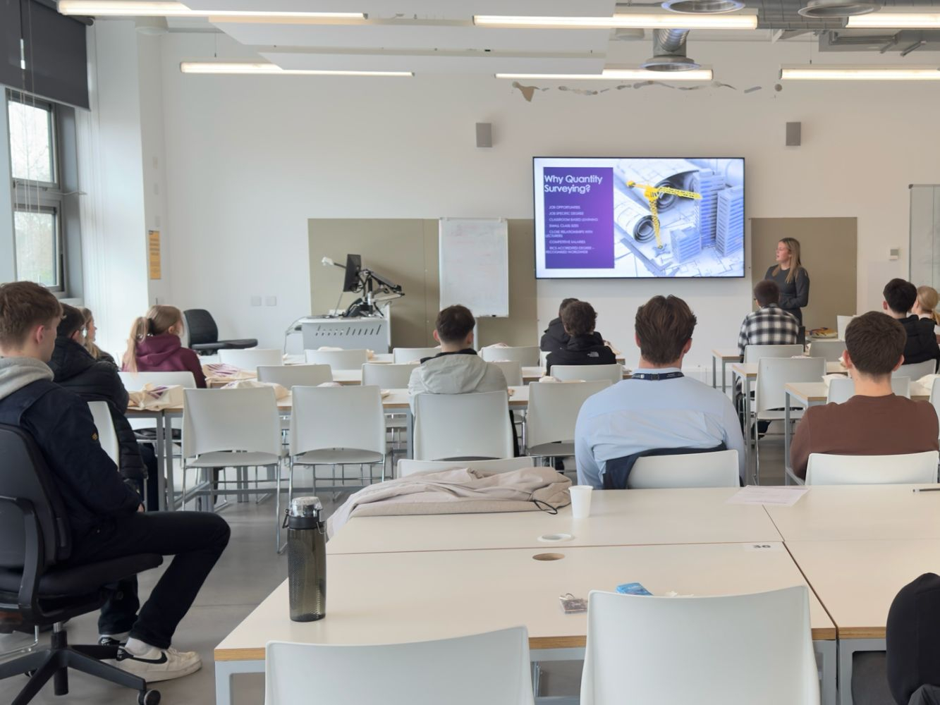 Prospective students watch one of the speakers, sat in a classroom looking towards a PPT