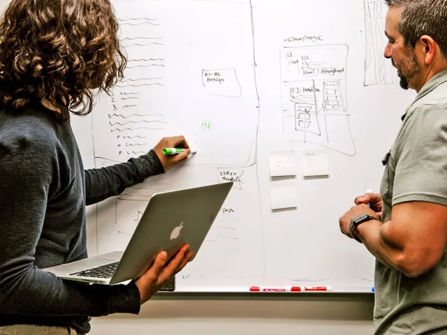 person holding a laptop and writing on a whiteboard