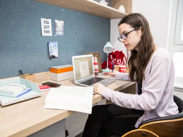 student sitting at desk with laptop looking at notes