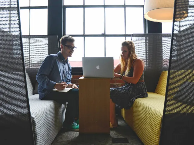 two people sitting in a booth looking at a laptop