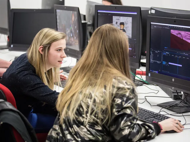 students chatting next to computer in Multimedia Lab