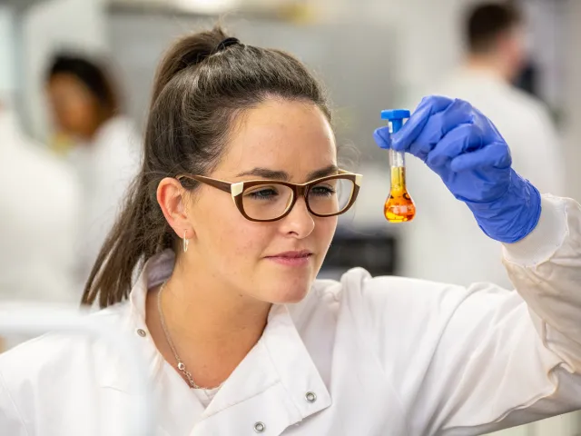 woman wearing protective gloves looking closely at a flask