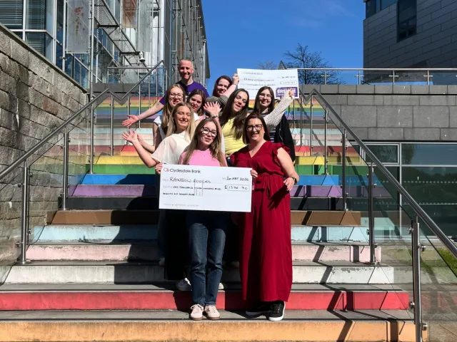 Events Management students on the RGU rainbow stairs holding two big cheques