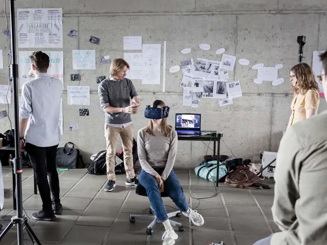 people in a creative workspace, one is wearing a VR headset