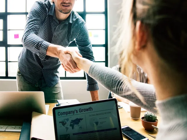 two people shake hands over their laptops on a table