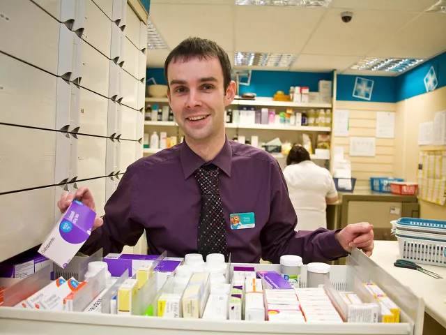 man in pharmacy showing a box of medicine to the camera