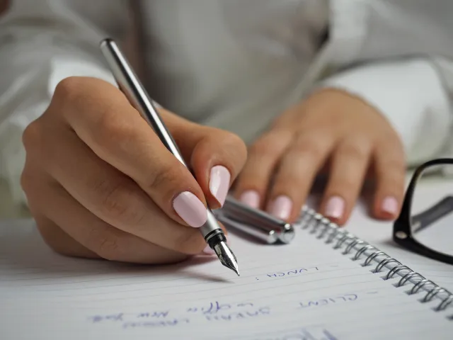 person with painted nails writing in a notebook