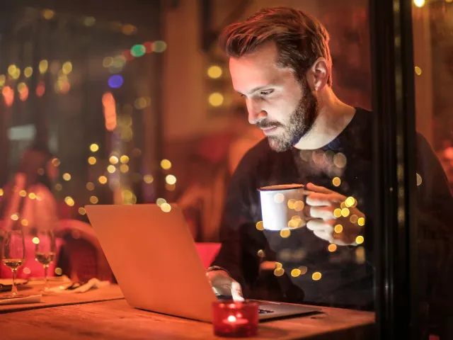 man in a cosy looking cafe holding a mug