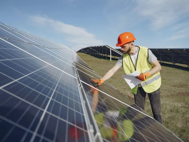 person in high-viz jacket and hard hat looking at solar panels in a field