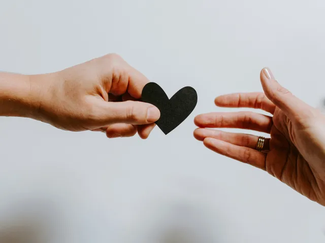 hand reaching for another hand with a paper cut out of a heart