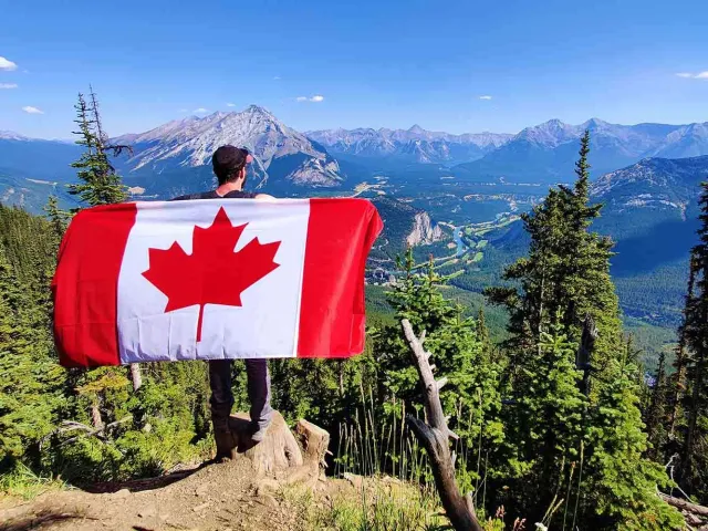 man holding canadian flag in front of mountainous vista