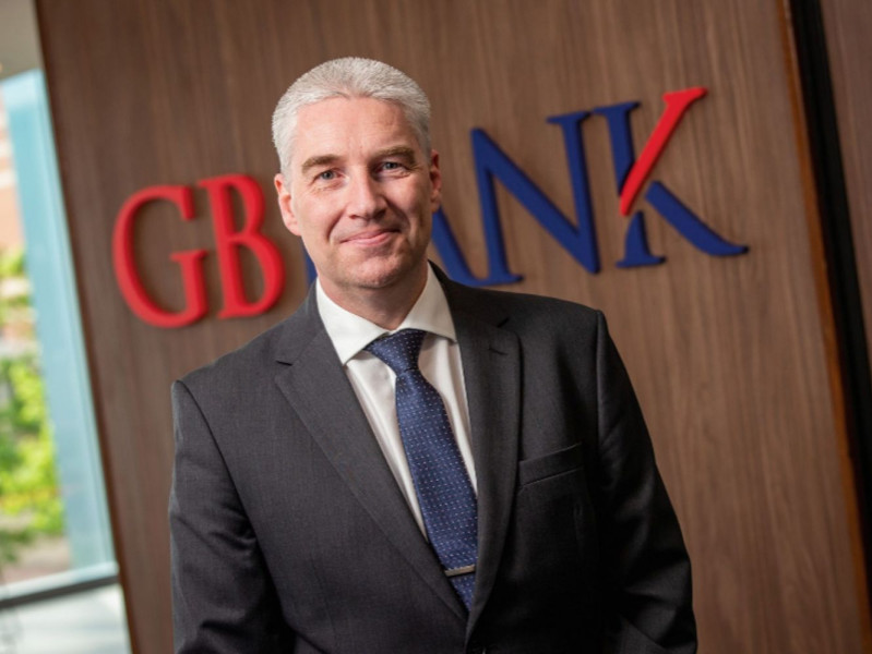 Stephen Lancaster with the logo of GB Bank on the wall behind him