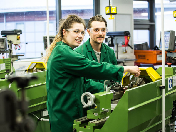 two students in engineering overalls at machines two students in engineering overalls at machines