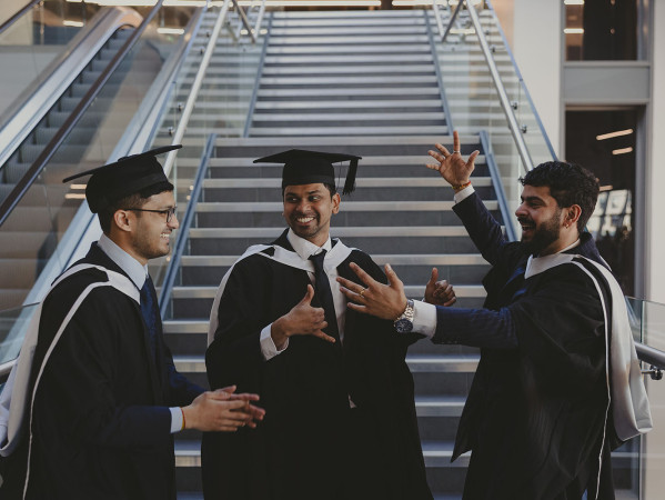 3 male graduates looking at one another cheerfully