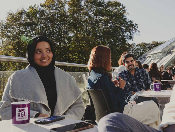 Students sitting in seating area outside Sir Ian Wood Building, student smiling and looking away from camera
