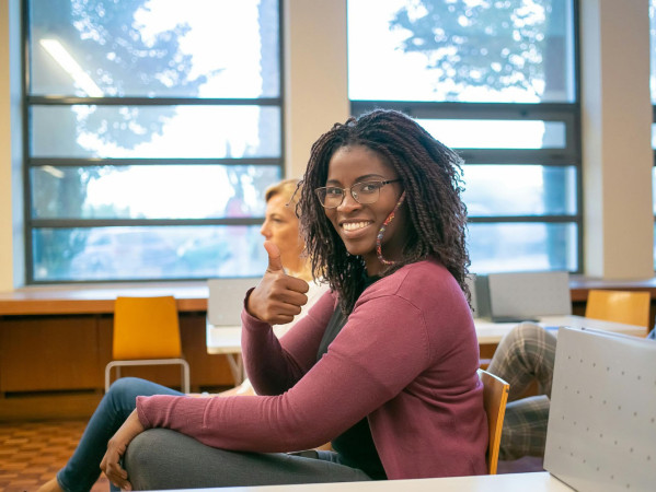 Woman sitting, looking at camera doing a thumbs up