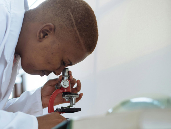 Person wearing lab coat looks into microscope