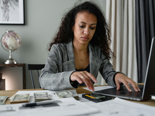 person at a laptop with a calcuator and cash