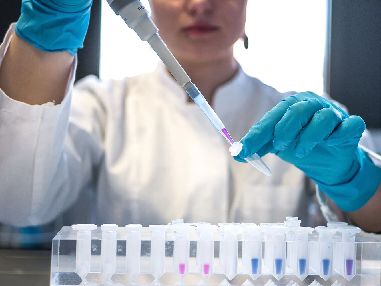 person in a lab coat and gloves using a pipette